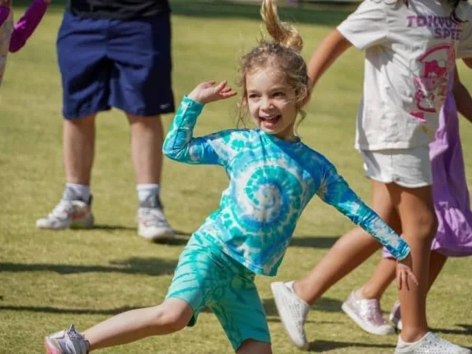 A camper in a tie-dye shirt dances on the grass