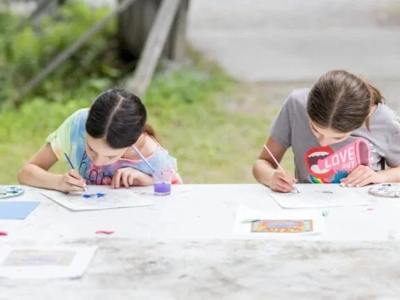 Two campers paint with watercolors at an outdoor table